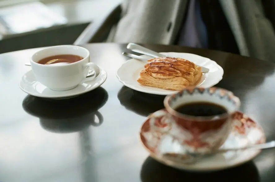 Image of a small table shown with cups of tea and coffee as well as a dish with a pastry.