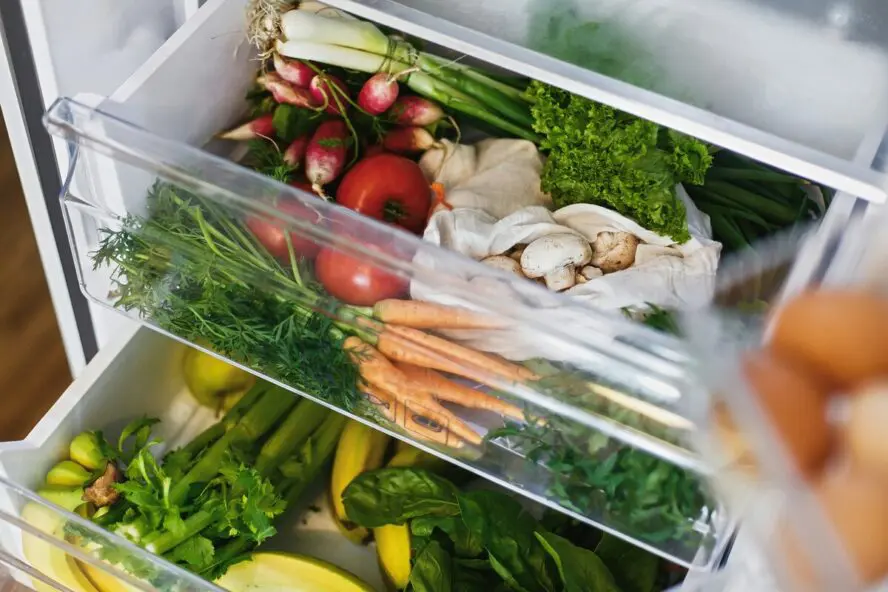 Image of two open crisper drawers in a refrigerator, stocked full of fresh vegetables.