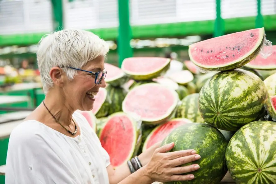 Image of a woman examining watermelon at a grocery store.