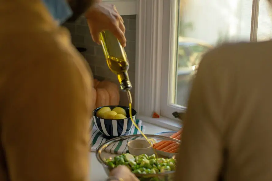 Image of someone pouring olive oil out of a bottle onto a dish, shot between two people.
