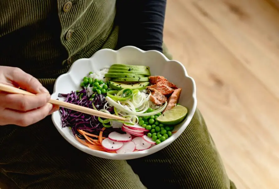 Image of someone eating a beautifully plated salmon rice bowl with chopsticks.