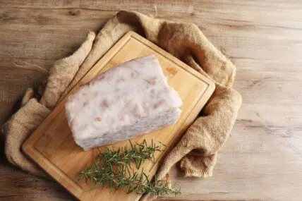 Image of a large block of beef tallow shown on a wooden cutting board next to a sprig of rosemary.