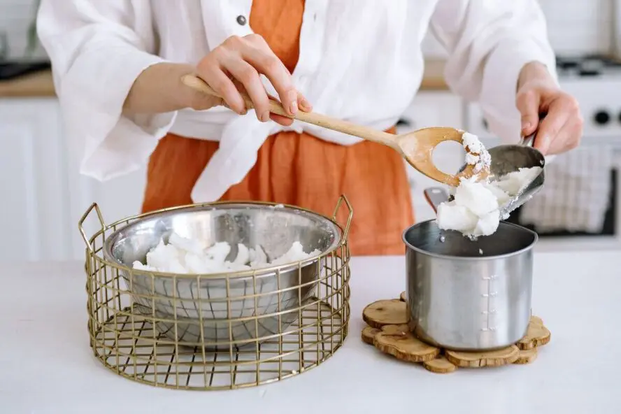 Image of a pair of hands working to separate out beef tallow from a larger bowl into a smaller pot.