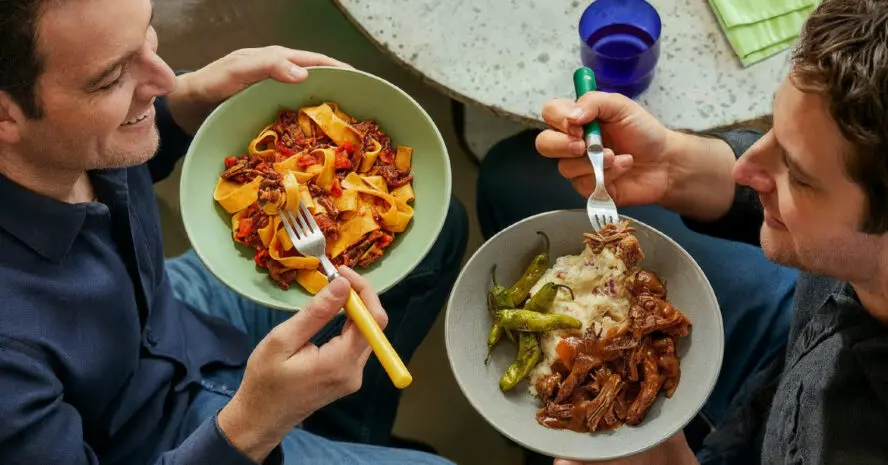 Image shot from above of two men enjoying CookUnity meals served on plates.