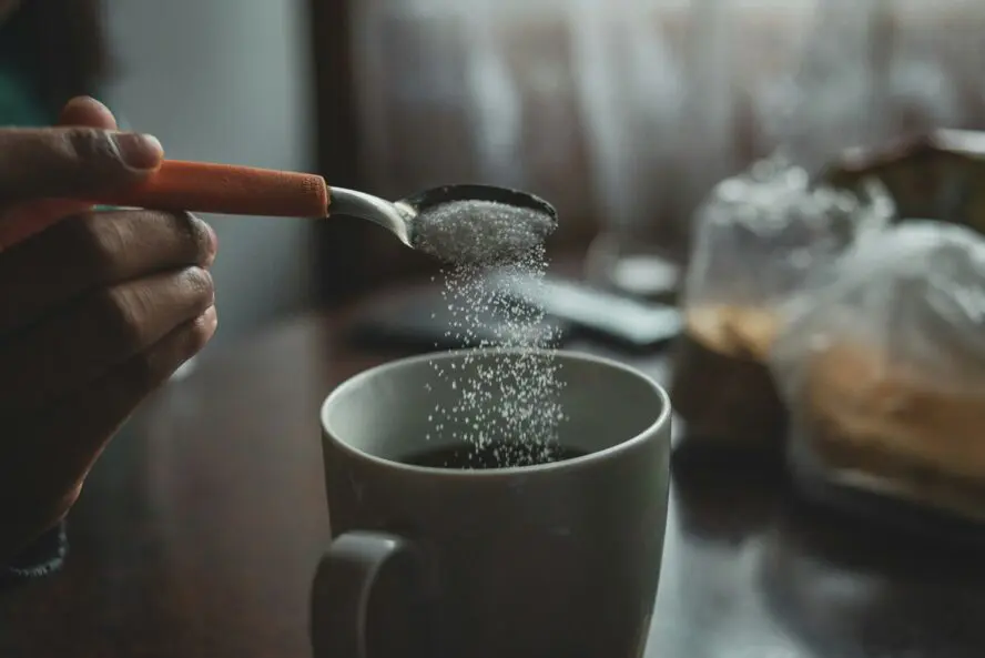 Image of someone holding a spoon of sucralose over a cup of coffee.