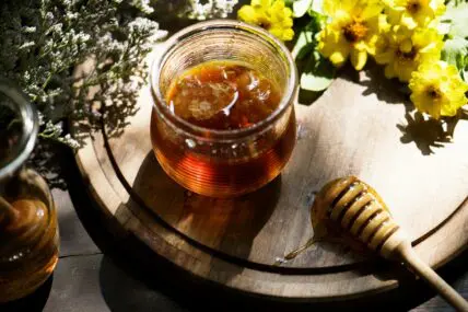 Image of a round wooden board with several wildflowers and a jar of organic honey.