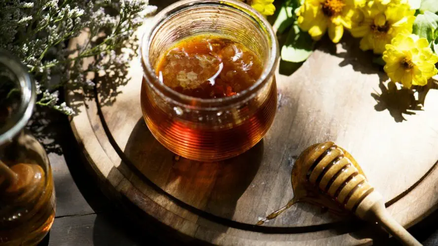 Image of a round wooden board with several wildflowers and a jar of organic honey.