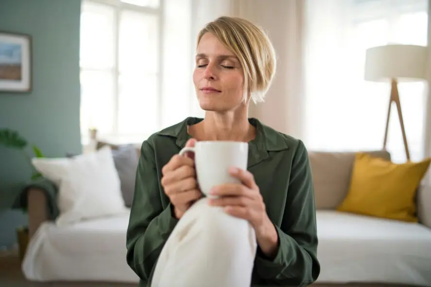 Image of a woman holding a mug with her eyes closed in meditation.
