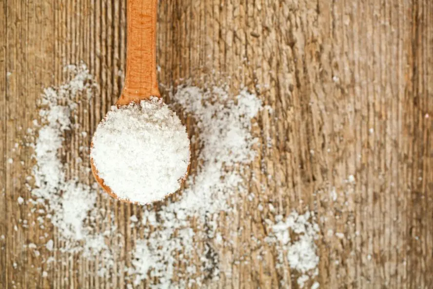 Image of a wooden spoon overflowing with sucralose, poured out on a table.
