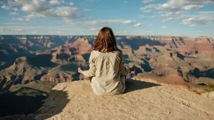 Image of a woman sitting cross-legged at the edge of a cliff and meditating.
