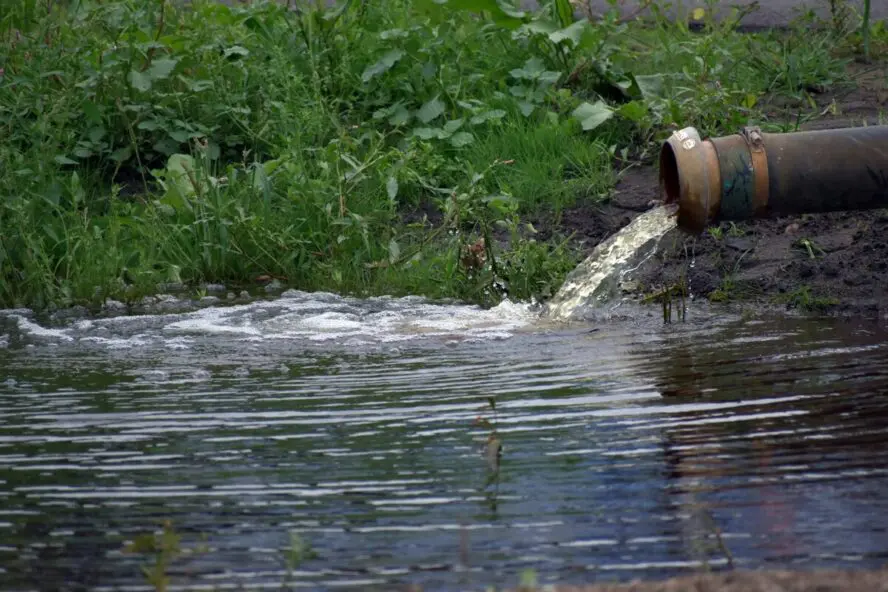 Image of a large pipe with water pouring out from it into a river.