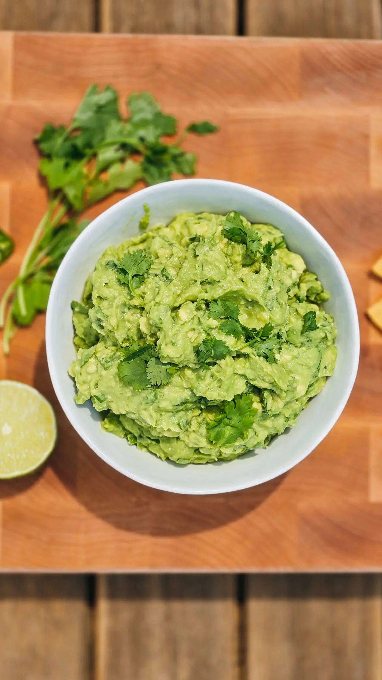 close up overhead view of guacamole served in white bowl with halved lime and sprigs of cilantro