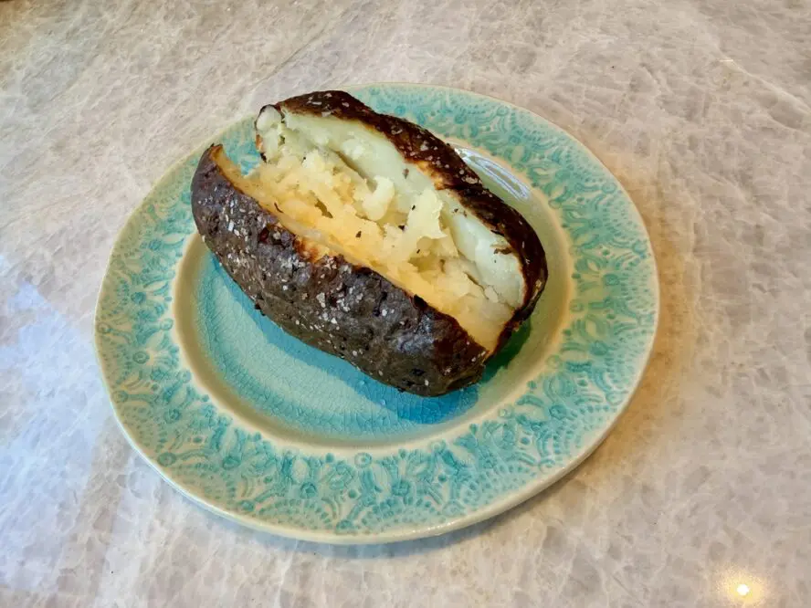 Image of a crispy air fryer baked potato, sliced open on a green plate.