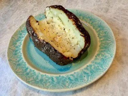 Image of a sliced open crispy air fried baked potato on a green ceramic plate.