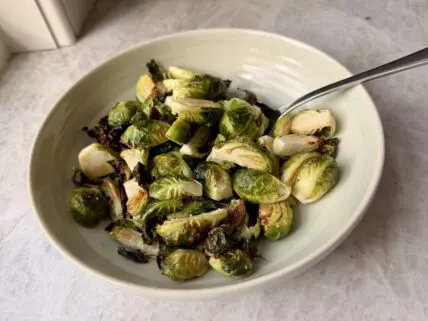 Image of a bowl of crispy air fryer Brussels sprouts, with a long spoon in the bowl for serving.