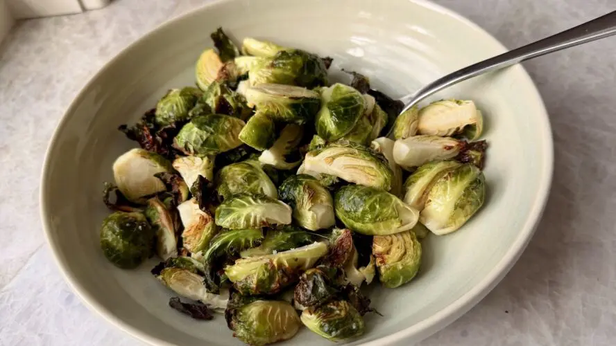 Image of a bowl of crispy air fryer Brussels sprouts, with a long spoon in the bowl for serving.