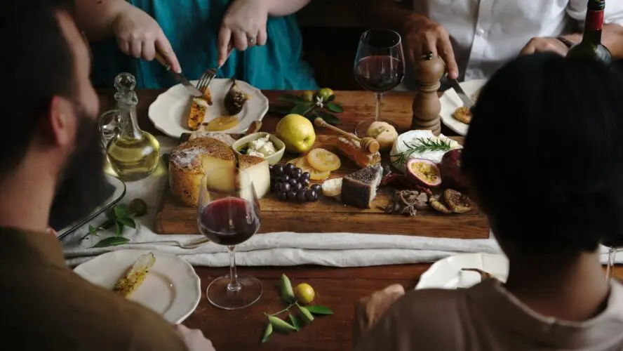 Image of a group of people sitting at a dinner table covered in various cheeses and glasses of red wine.