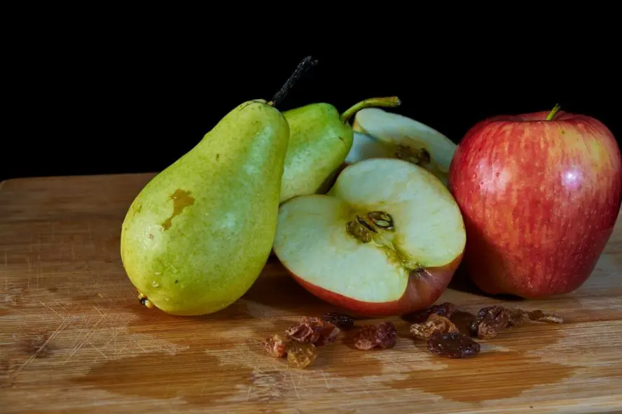 Moody shot of a wooden cutting board with two pears and a couple of apples sliced in half.