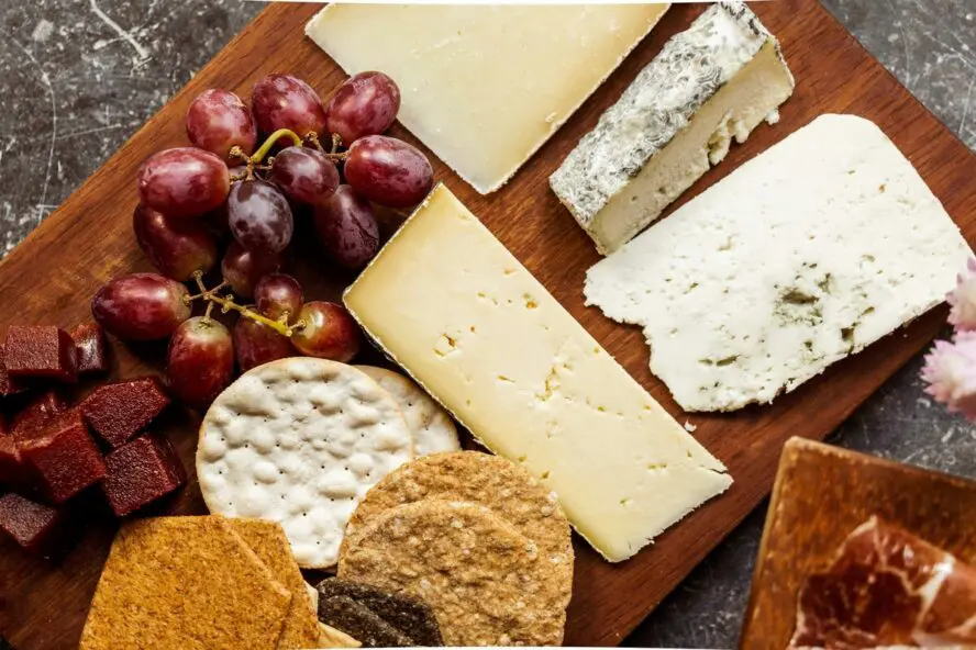 Image of a wooden board topped with various wedges of cheese, grapes, and crackers.