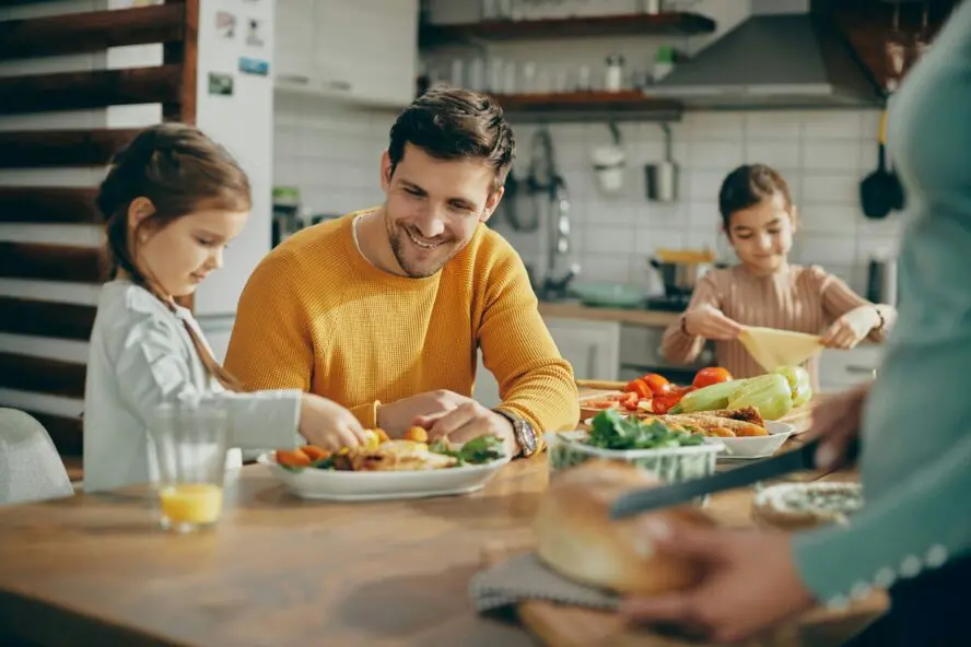 Image of a young father and his kids sitting at a table eating a meal together.