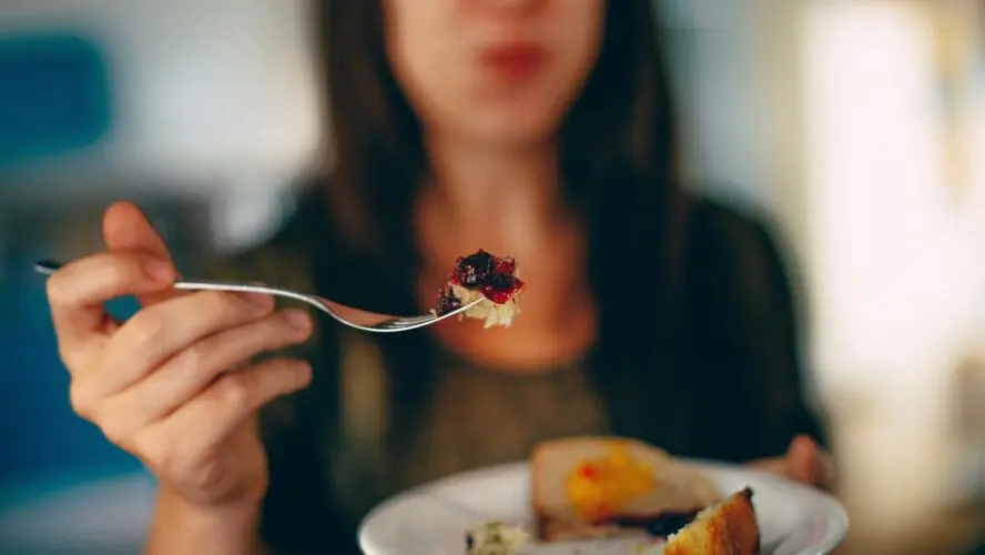 Image of a woman holding out a fork with some food on it.