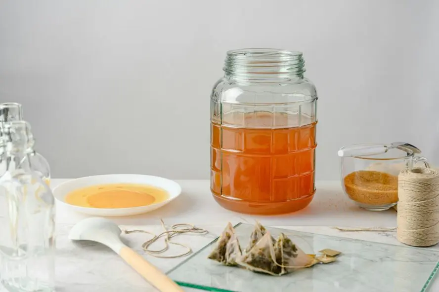 Image of a large mason jar being used to make homemade kombucha, with several tea bags discarded beside it.