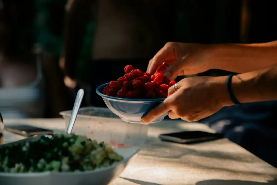 a hand reaching in a bowl of fresh summer raspberries which double for skin hydration.
