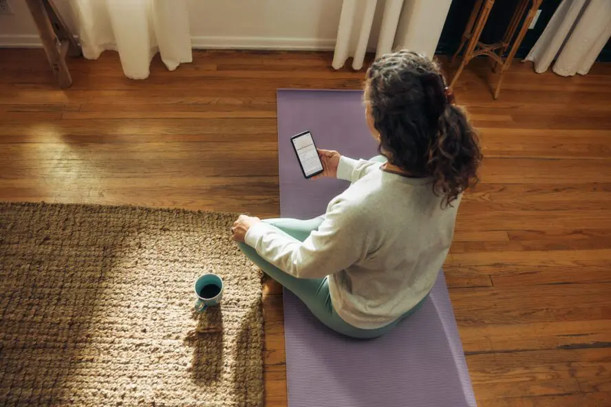 woman on yoga matt sitting cross-legged holding phone