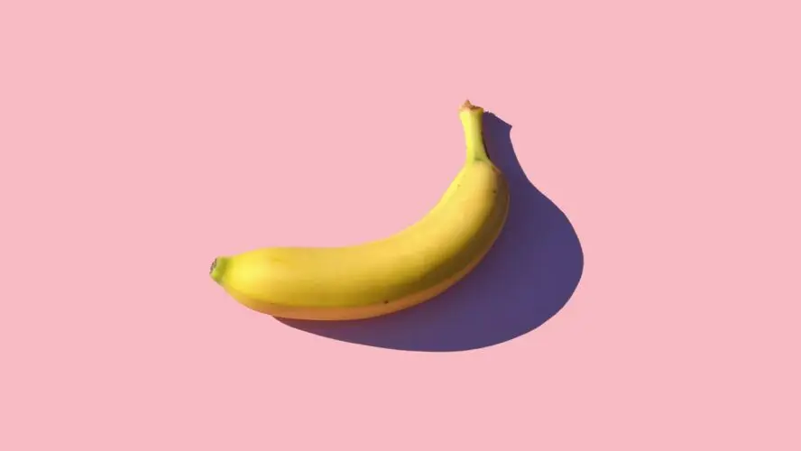 Image of a single ripe banana set against a light pink backdrop.