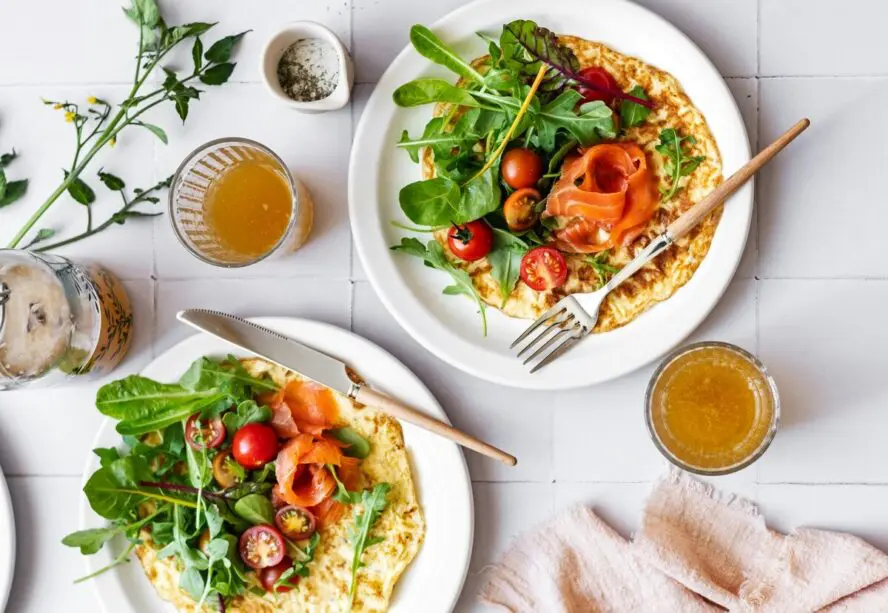 Image of two full plates with open-faced omelettes, smoked salmon, arugula, and tomatoes.