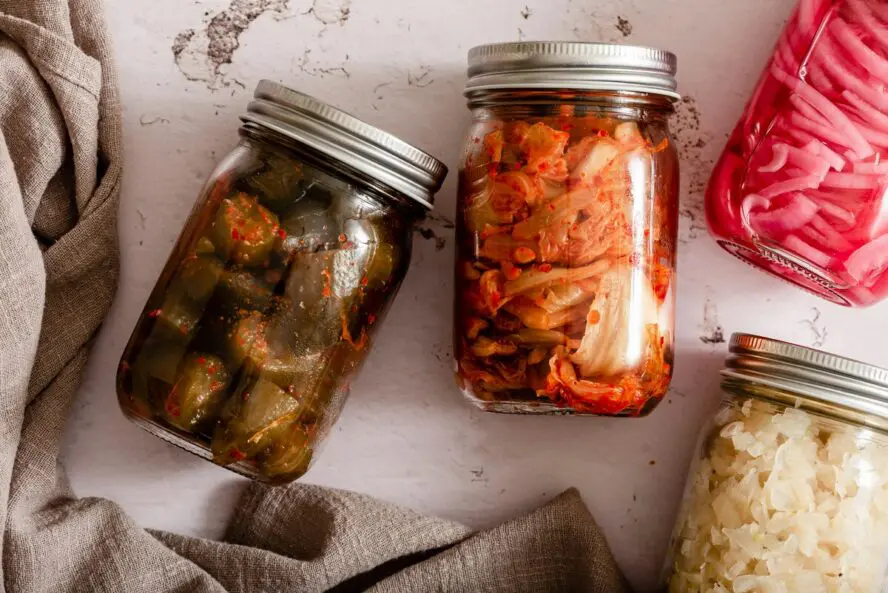 Image of several glass Mason jars full of fermented foods lying on their sides, including kimchi and pickled vegetables.