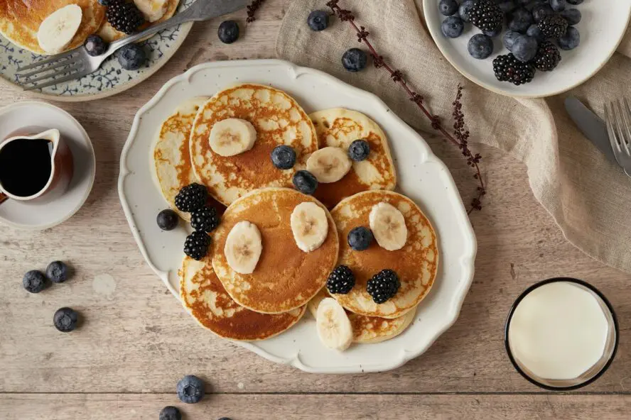 Image of a pile of banana pancakes, topped with slices of banana and blueberries.