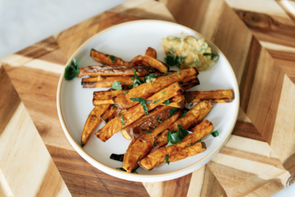 overhead view of sweet potato fries from an air fryer on a white plate on a wood cutting board.