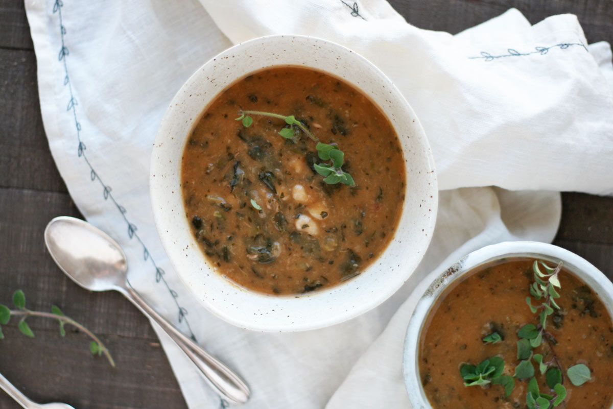 This recipe for turkey leftovers is a white bean, turkey, and kale soup. Pictured in pretty white bowls with a napkin and spoon.