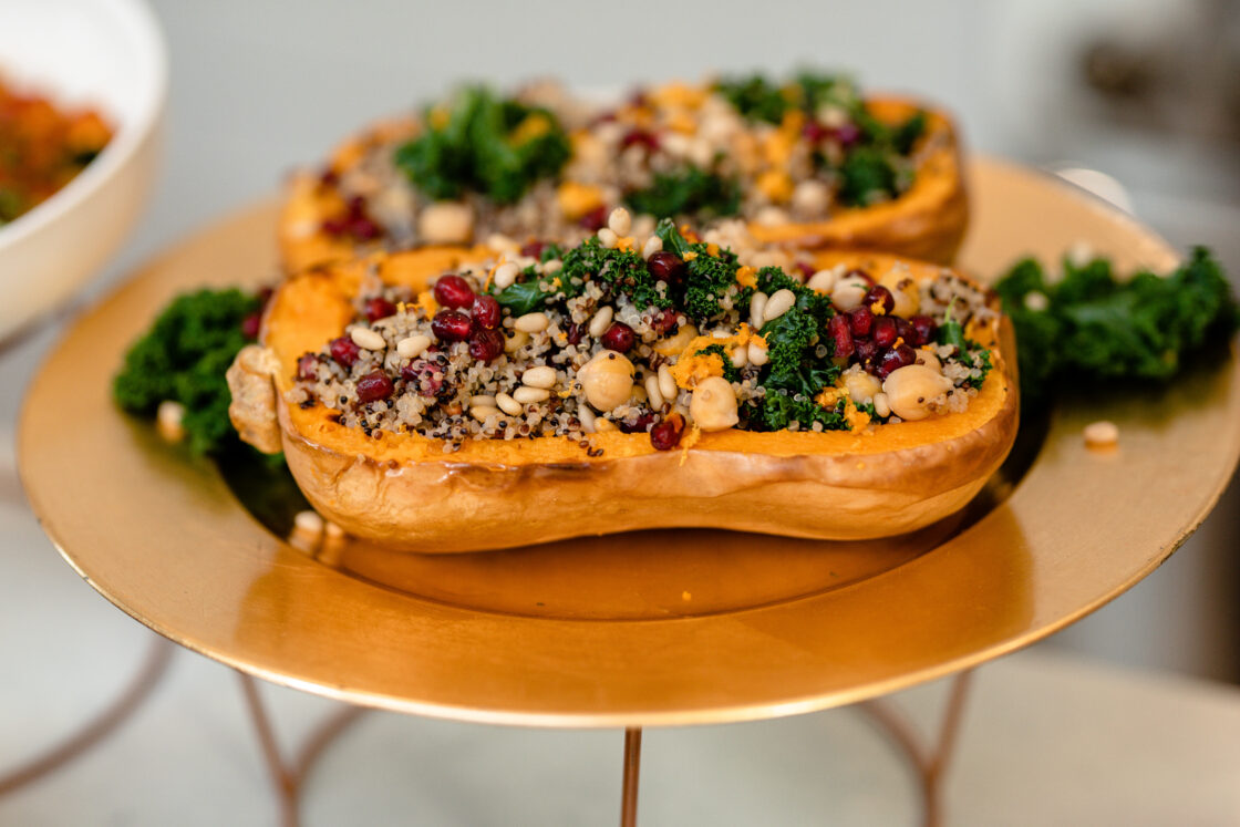 vegan stuffed butternut squash stuffed with quinoa and pine nuts served on a gold plate
