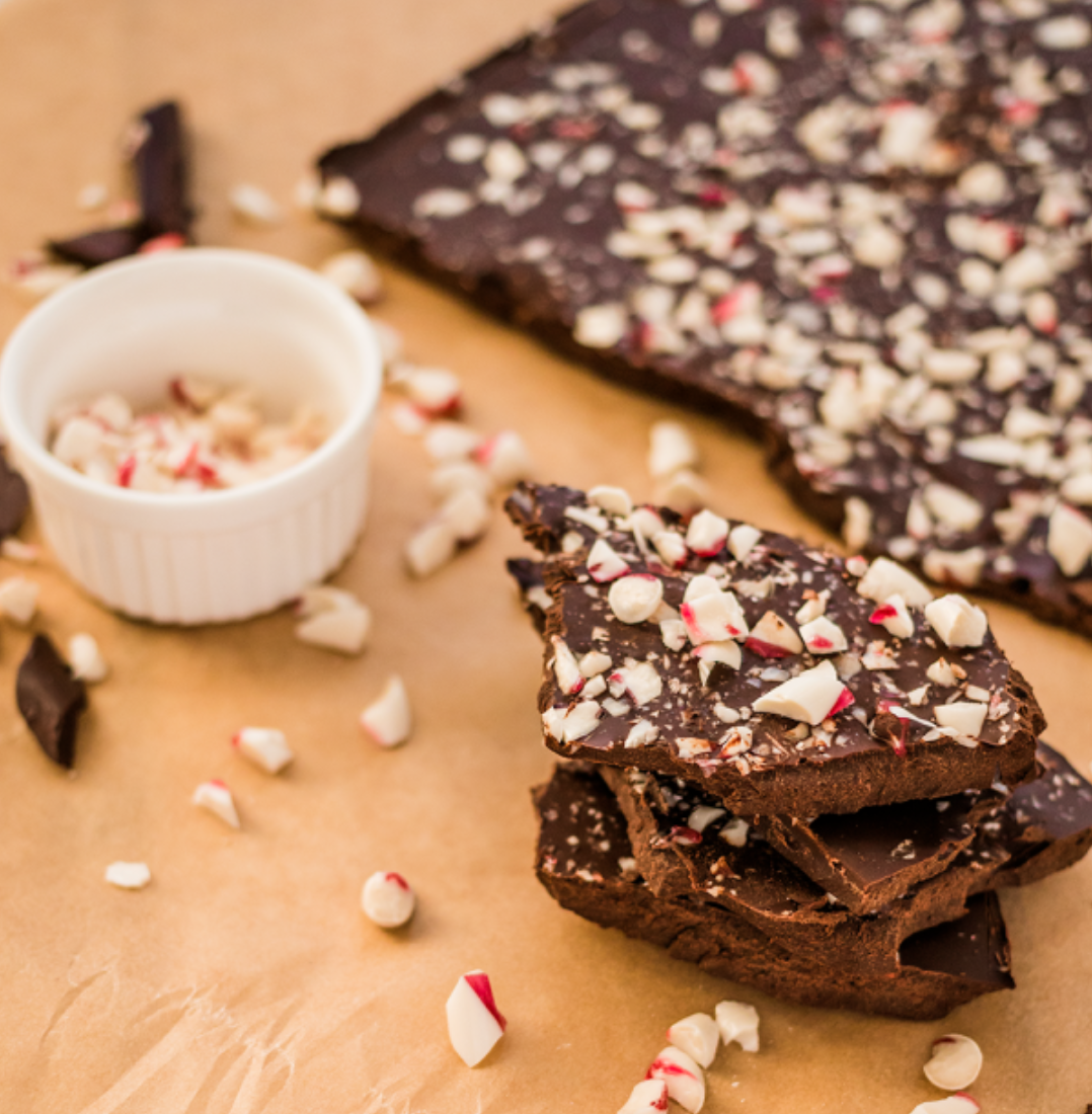 Image of chocolate peppermint bark recipe served on unbleached parchment with crushed peppermint candy sprinkled around, this dessert is so easy to throw together last minute to bring to a holiday function or give as a gift.