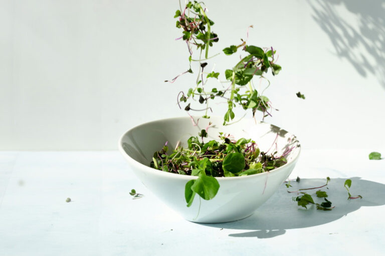 Broccoli sprouts being tossed in a salad bowl