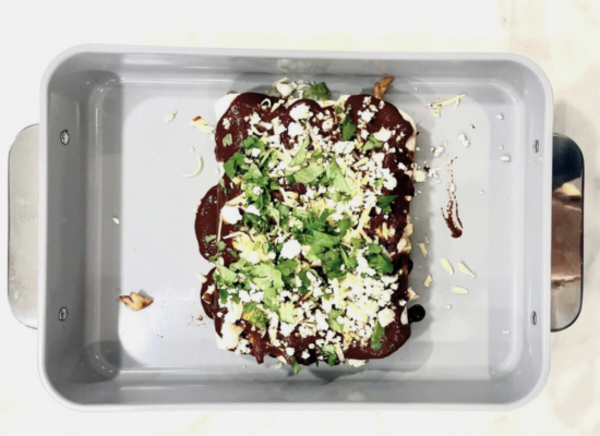 Image of enchiladas in served in Caraway Home's non-stick bakeware, served with cilantro and cotija cheese, on a plain white background.