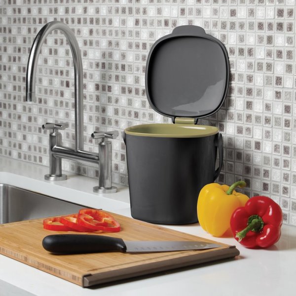 Black countertop compost bin with knife and fresh vegetables on kitchen counter