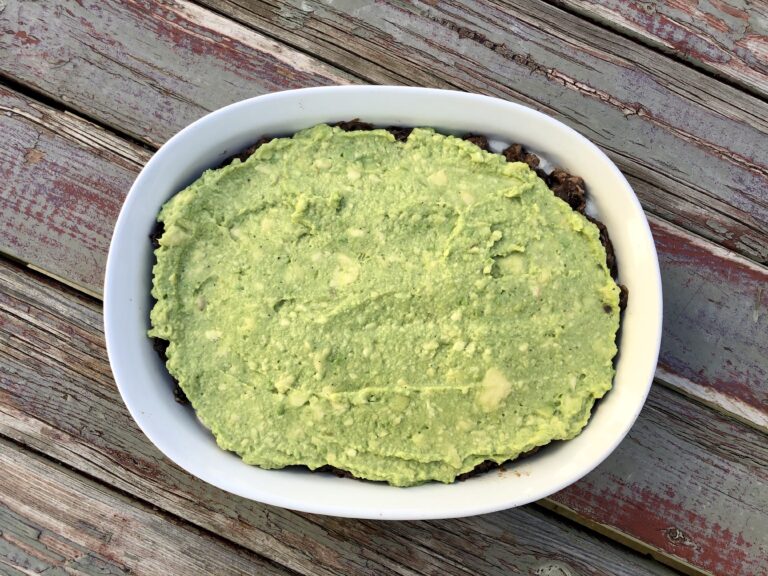 image of an overhead shot of guacamole as the third layer of a healthy vegan black bean layer dip