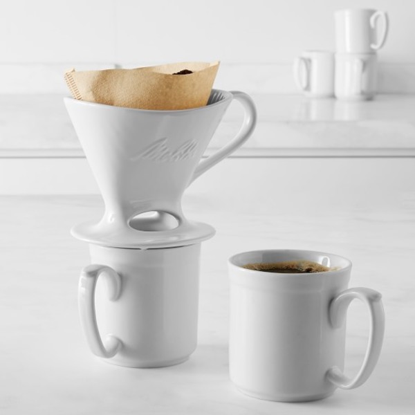 White ceramic pour-over coffee dripper with filter and mug of brewed coffee