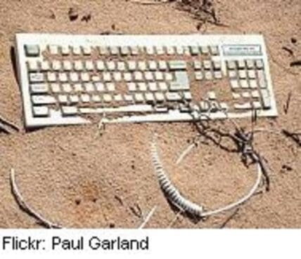 Discarded computer keyboard and cables on sandy ground