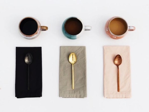 Three coffee cups with matching spoons on colored napkins arranged in rows.