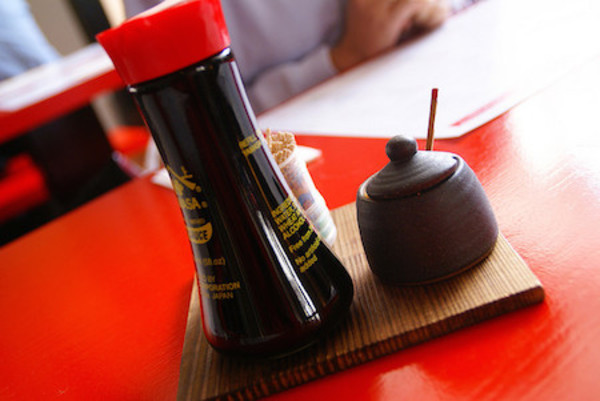 Bottle of soy sauce with brush and small ceramic dish on red surface