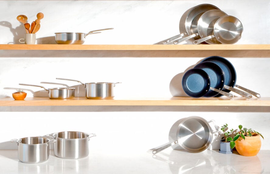 Image of Made In's professional cookware stacked on various shelves in a bright kitchen.