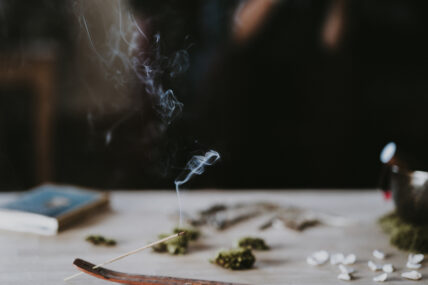 Image of incense burning safely in the foreground, with various wholistic, meditative items on the table behind with a journal showing that you can burn incense safely.
