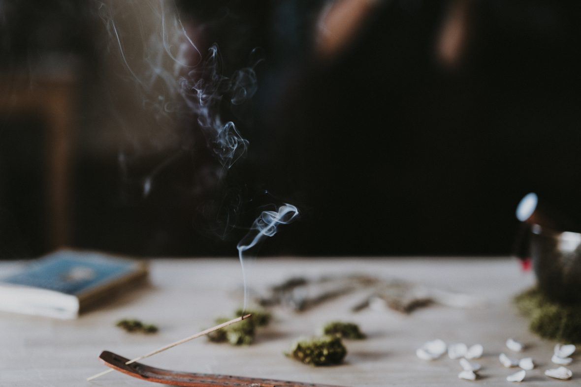 Image of incense burning safely in the foreground, with various wholistic, meditative items on the table behind with a journal showing that you can burn incense safely.