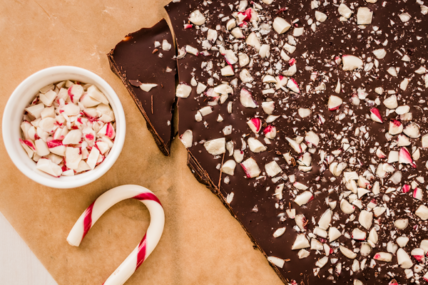 Image of 4-ingredient vegan chocolate bark recipe served on unbleached parchment paper with a small white ramekin filled with crushed peppermint candy and striped candy cane.