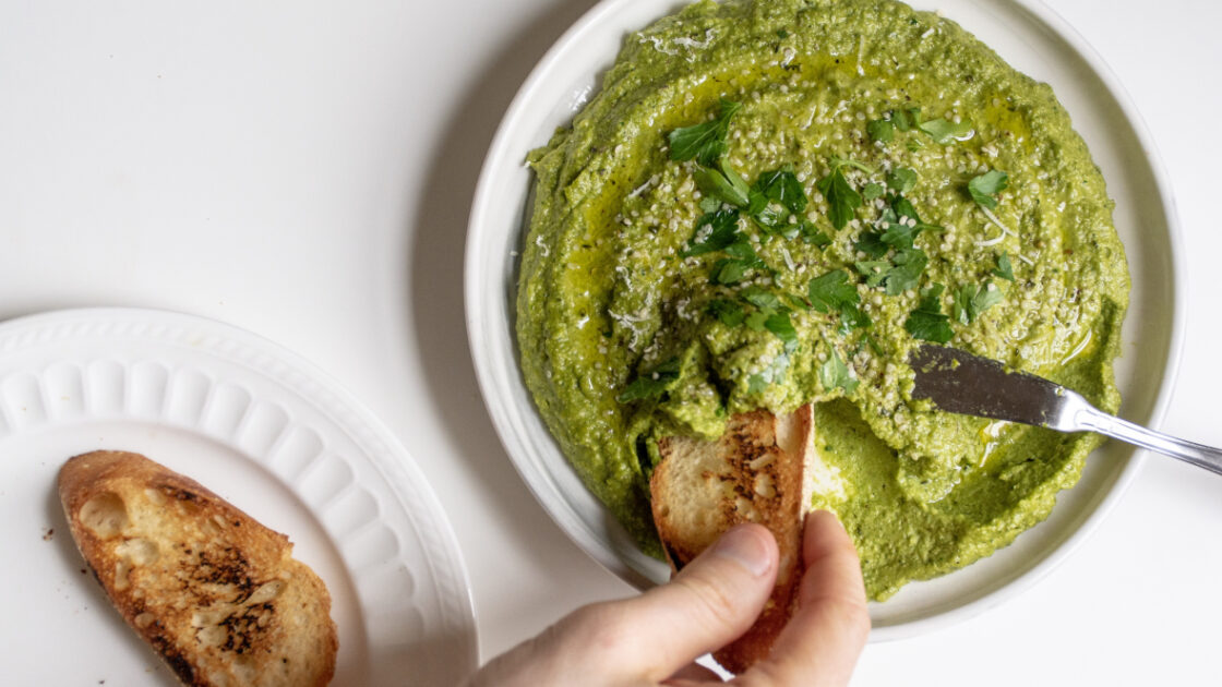 hand holding toast dipping into Fava Bean Pesto