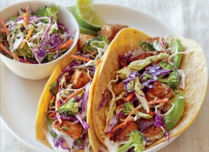 Image of two fish tacos with slaw made with broccoli and served with a tangy lime crema.